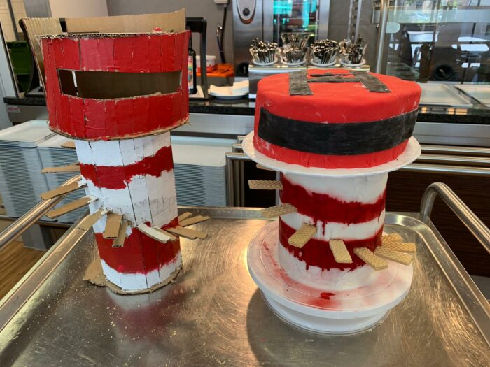 Zwei rot-weiß gestreifte Leuchtturm-Modelle aus Karton und Waffeln auf einem Metalltablett in einer Küche.